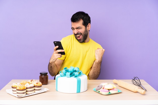 Man in a table with a big cake with phone in victory position