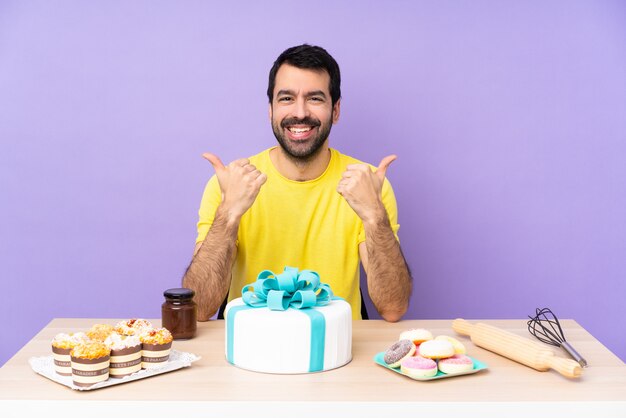 L'uomo in una tabella con una grande torta con i pollici aumenta il gesto e sorridere