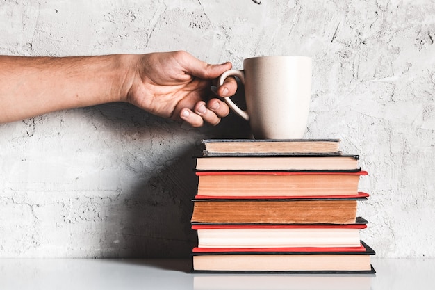 Un uomo prende il caffè da una pila di libri. istruzione, apprendimento, lettura, hobby