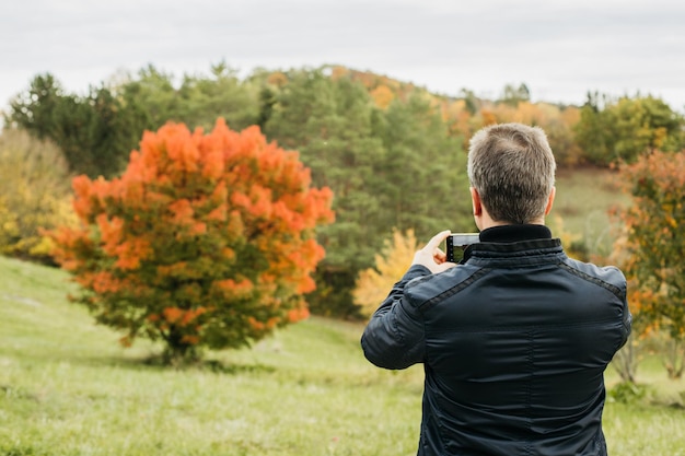 Photo a man takes a photo of a beautiful landscape a tree in an autumn park for his blog travel