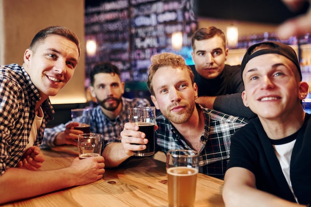 Man takes selfie by phone group of people together indoors in
the pub have fun at weekend time