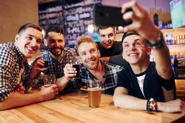 Man takes selfie by phone Group of people together indoors in the pub have fun at weekend time