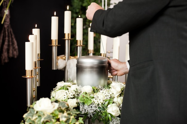 man taking funeral urn with candles and flowers