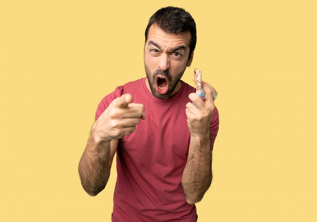Man taking a lot of money frustrated by a bad situation and pointing to the front on isolated yellow background