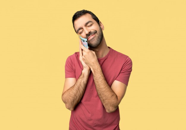 Man taking a lot of money making sleep gesture in dorable expression on isolated yellow background