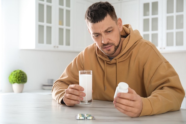 man taking medicine for hangover at table in kitchen