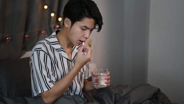 Man taking medicine pills while sitting in the bed.