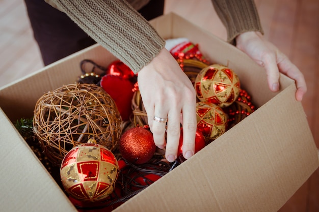 A man taking out a christmas ball from the cardboard box with toys for Christmas tree ornaments