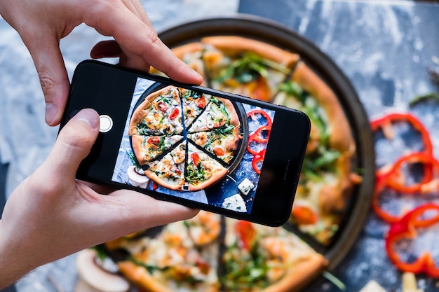 Man taking photo of pizza with smartphone Closeup view of process