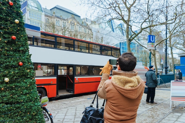 Uomo che scatta foto del bus turistico del tour della città sul suo telefono cellulare a berlino, germania.