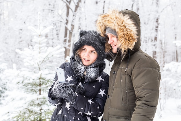 セルフィー写真を撮る男若いロマンチックなカップルは雪の森の屋外の冬を笑顔します。