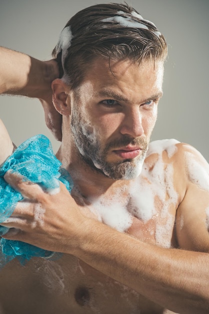 Photo man taking shower with sponge and foam muscular man washing himself with soap sexy handsome man