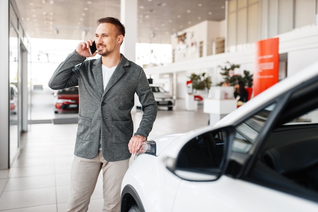 ショールームの新車の近くで電話で話している男性。