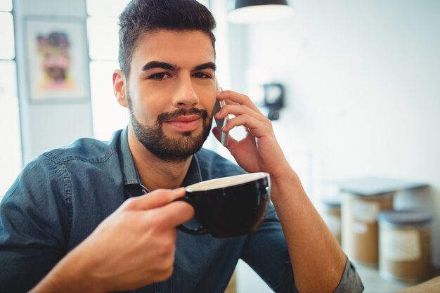 コーヒーを飲みながら携帯電話で話している男性