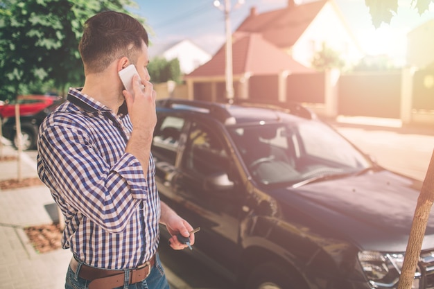 写真 携帯電話で話し、彼の車を見ている男