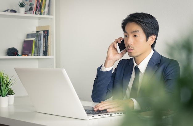 写真 テーブルの上のラップトップで携帯電話で話している男性