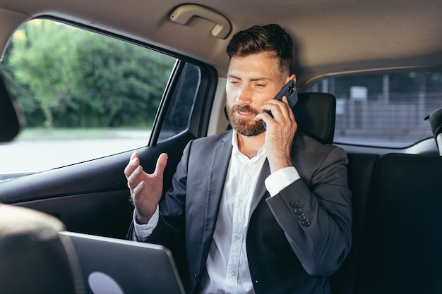 Man talking on the phone sitting in the car working with a laptop