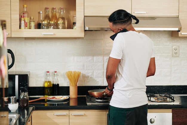 朝食を調理するときに電話で話している男、後ろからの眺め