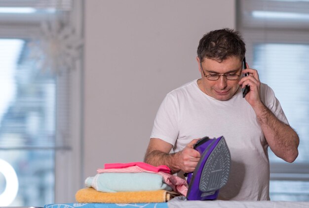 Photo man talking on phone while holding iron at home