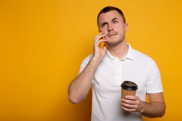 Man talking on smartphone with coffee to go on yellow