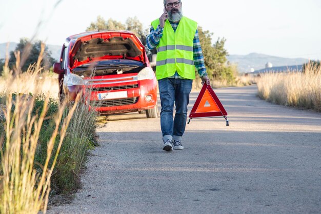 Photo a man talks on the phone while putting a warning triangle behind his vehicle.