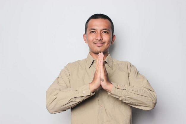 A man in a tan shirt is praying with his hands together.