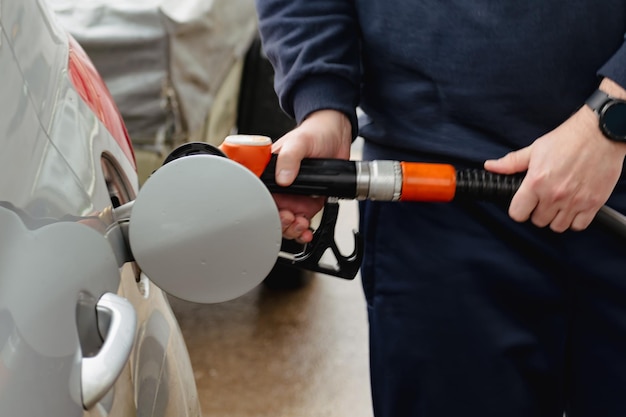 Man tankt een auto in Europa met een pistool in zijn hand Benzinestation tankt diesel en benzine De man vult een tank van een zilveren auto met brandstof