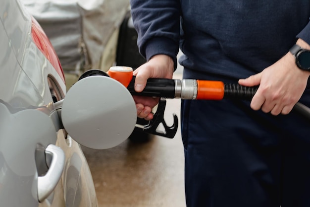 Man tankt een auto in Europa met een pistool in zijn hand Benzinestation tankt diesel en benzine De man vult een tank van een zilveren auto met brandstof