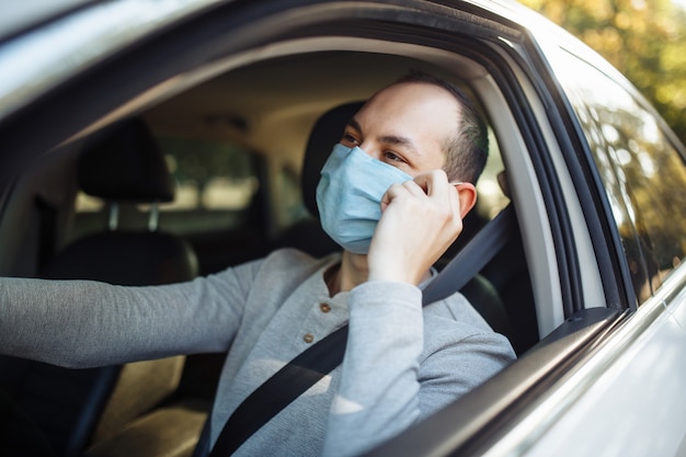 A man taxi driver drives a car and adjusts medical mask during coronavirus outbreak.