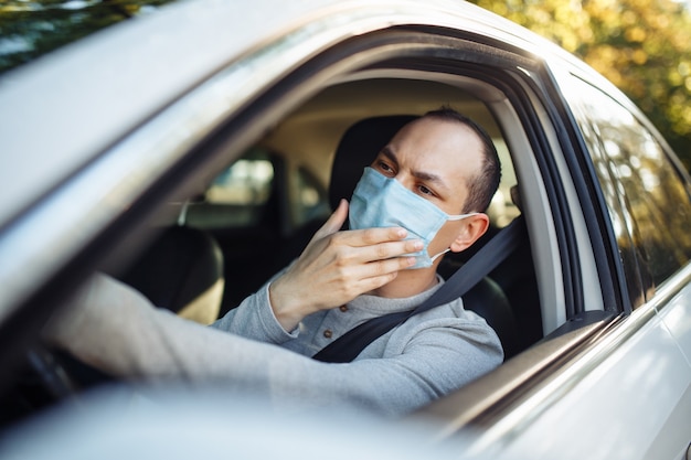 A man taxi driver drives a car and adjusts medical mask during coronavirus outbreak.