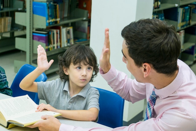 Man teacher and kid student learn with book at bookshelf