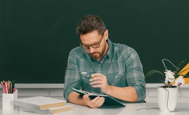 Man teacher with books young professor on lesson at college teacher writing text near chalkboard in