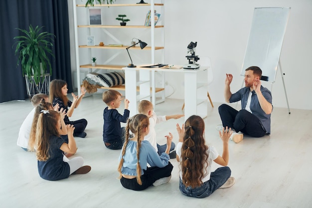 Man teaches gesture language group of children students in\
class at school with teacher