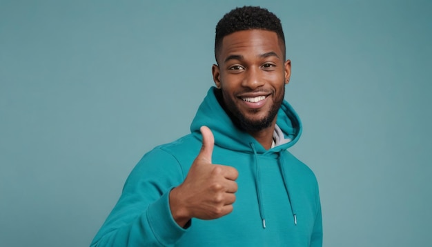 Photo a man in a teal hoodie giving a thumbs up with a confident smile on a teal backdrop