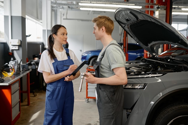 Man technician and woman mechanic talking at car service garage