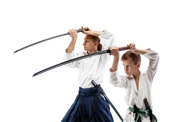 Man and teen boy fighting at Aikido training in martial arts school. Healthy lifestyle and sports concept. Fighters in white kimono on white wall. Karate men with concentrated faces in uniform.