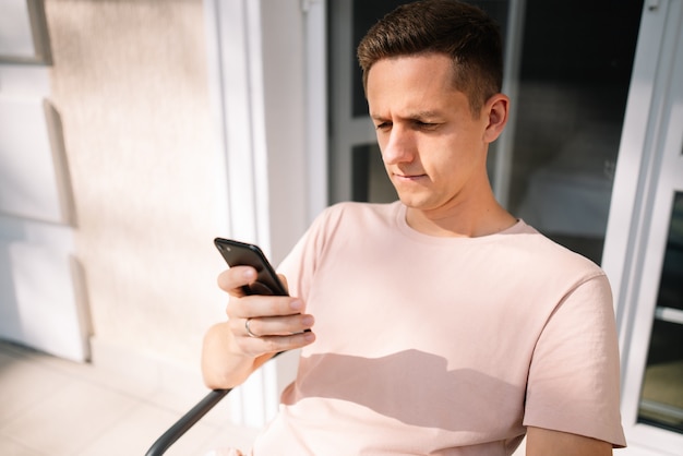 Man texting on mobile phone sitting on a chair in the balcony close up