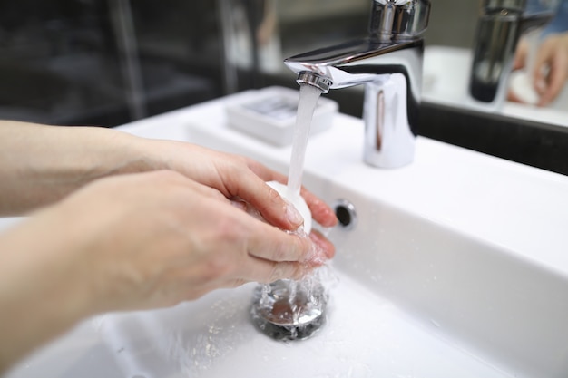 Man thoroughly washes his hands with soap under tap