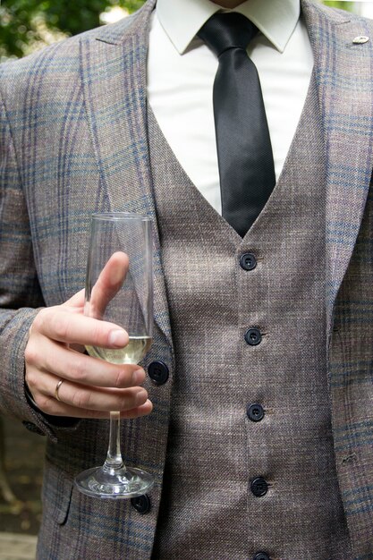 Мужчина в костюме-тройке держит бокал, чтобы закрыть Рука человека держит бокал белого вина