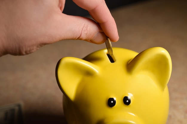 Man throwing coins into a piggy yellow piggy bank