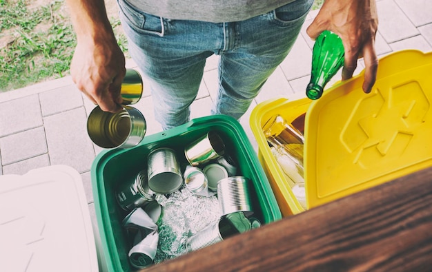 Foto uomo che getta la bottiglia di vetro e il barattolo di latta in diversi bidoni della spazzatura per lo smistamento dei rifiuti
