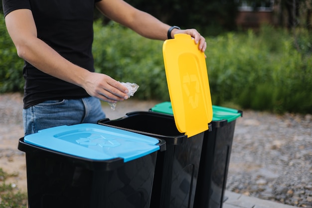 Man throwing plastic bag into recycling bin on back yard close up of humen hand hold rubbish