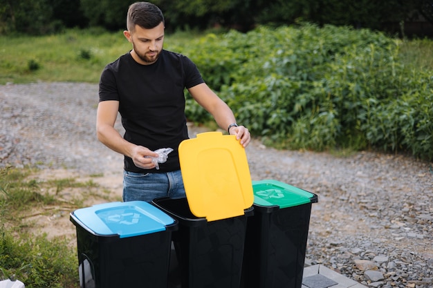 Uomo che getta un sacchetto di plastica nel cestino per il riciclaggio nel cortile sul retro di diversi colori sui bidoni di plastica verde