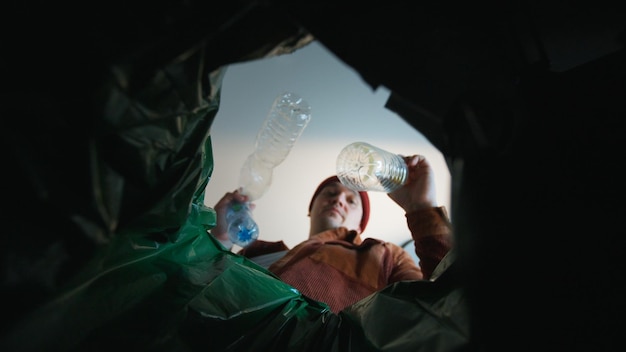 Foto uomo che getta una bottiglia di plastica in un bidone della spazzatura vista dal fondo del concetto eco del bidone delle spazzature