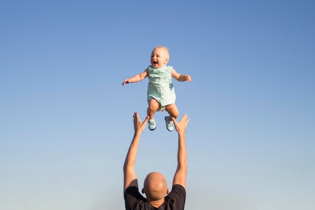 Man throws baby up against the blue sky. Concept game with children, happy family.