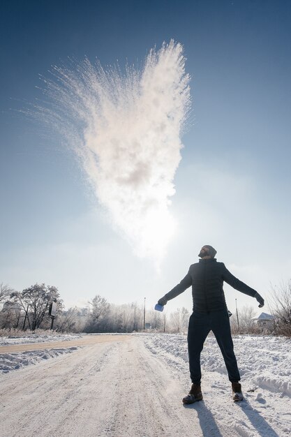 Foto un uomo butta fuori acqua bollente al freddo, che si trasforma istantaneamente in vapore. il trucco dell'acqua calda.