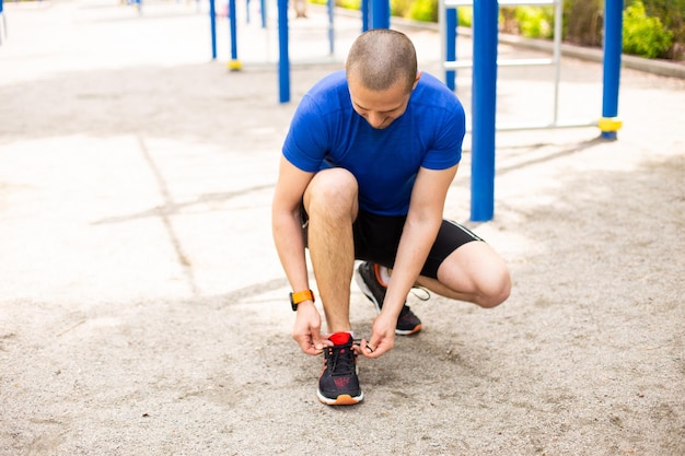 男はスポーツグラウンドでのトレーニングの前にスニーカーで靴ひもを結ぶ