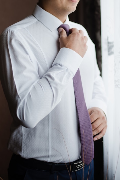 Photo man tightens tie purple tie groom in white shirt grooms fees