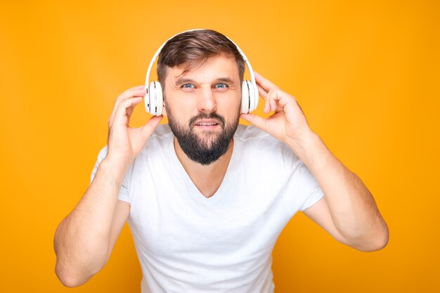 A man, tightly pressing musical headphones to his ears, and looking at the camera.