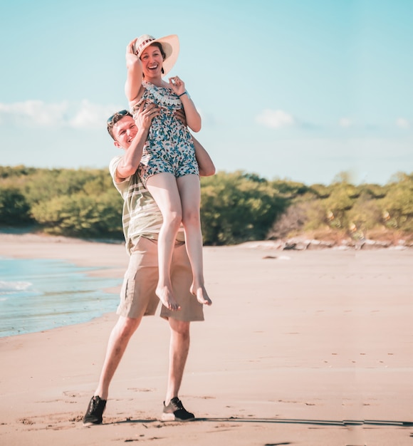 Man tillen vrouw op het strand in de lucht, man lacht blij met een vrouw op het strand, levensstijl van gelukkige man en vrouw op het strand